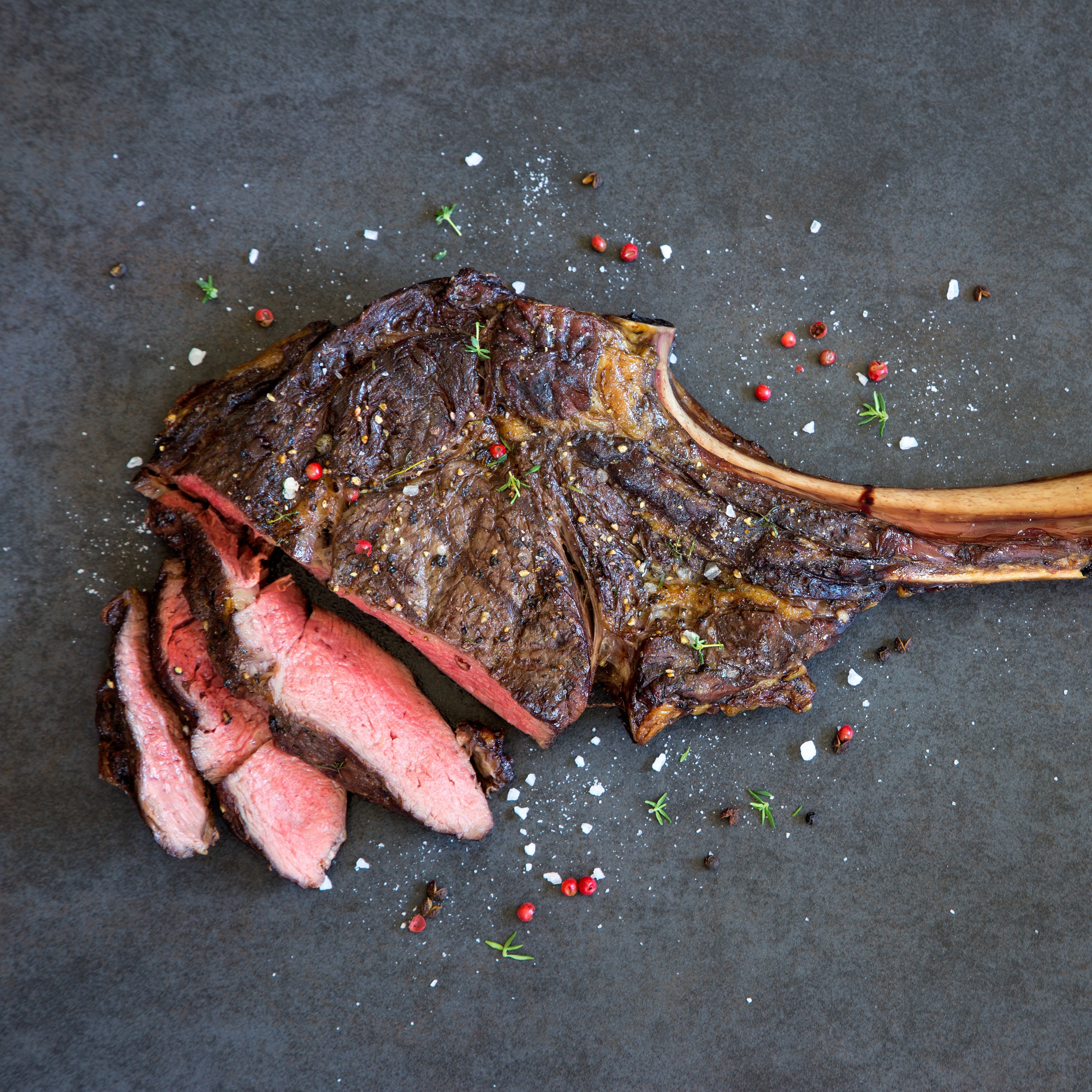 Grilled steak with a bone on a dark surface with spices