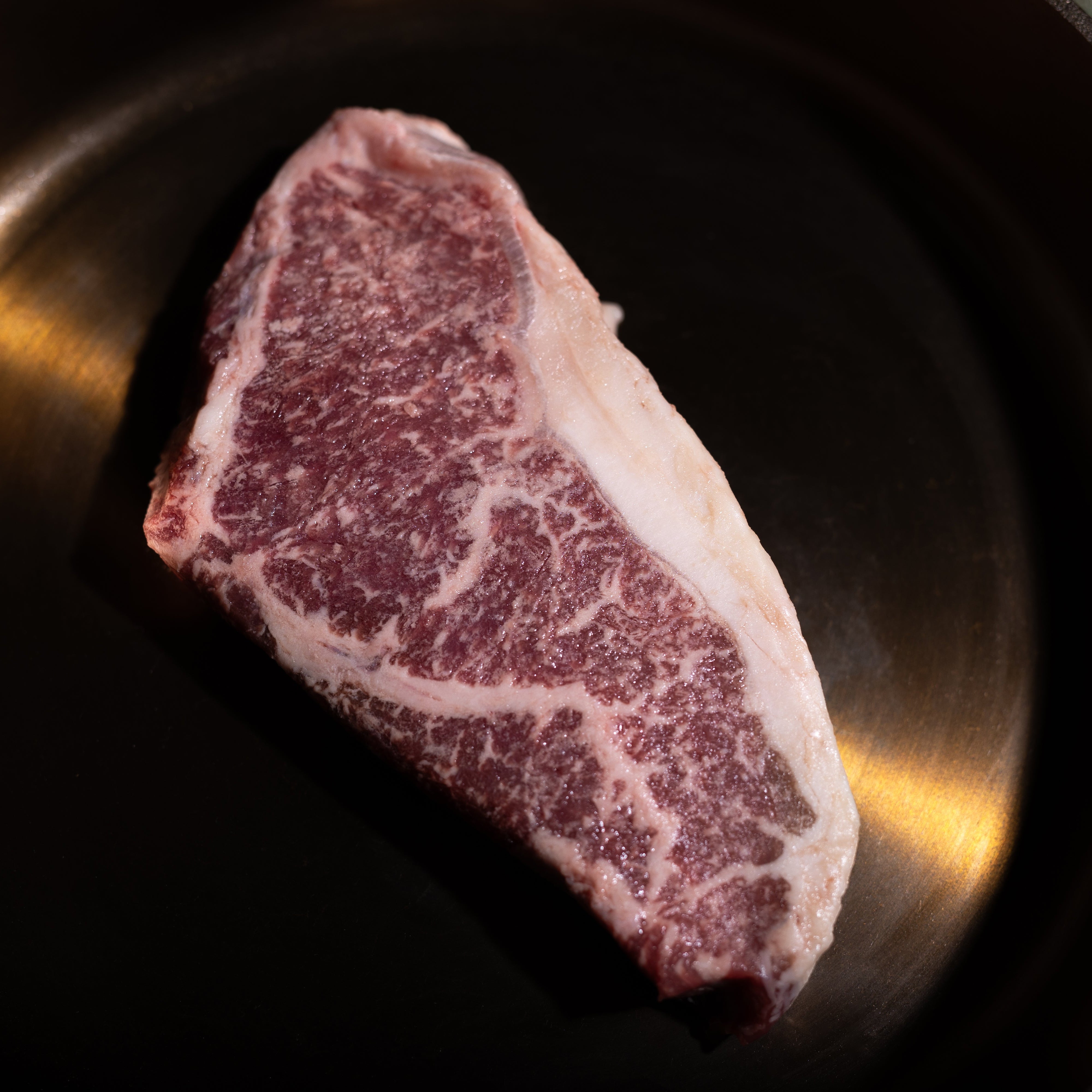 A raw marbled steak, likely a Wagyu cut, resting inside a dark cast iron skillet.