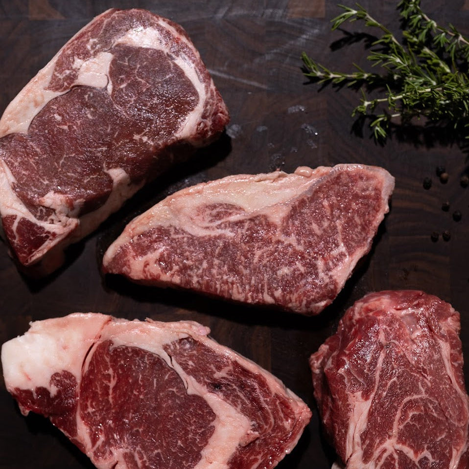 Raw wagyu beef steaks on a dark wooden cutting board with herbs and salt.