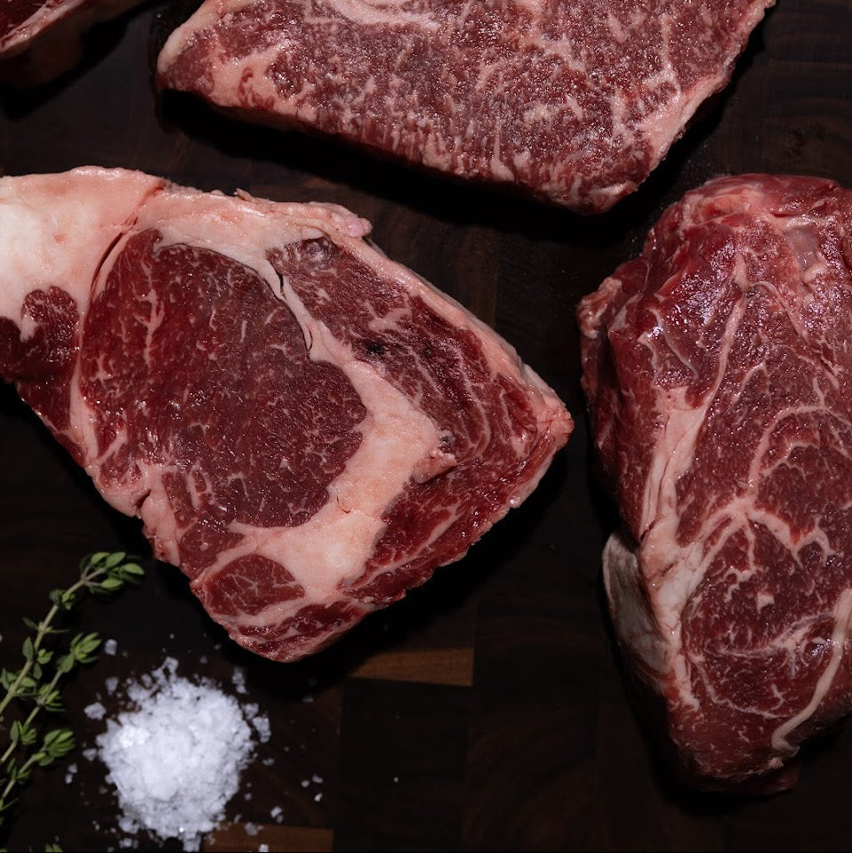 Raw wagyu beef steaks on a dark wooden cutting board with herbs and salt.