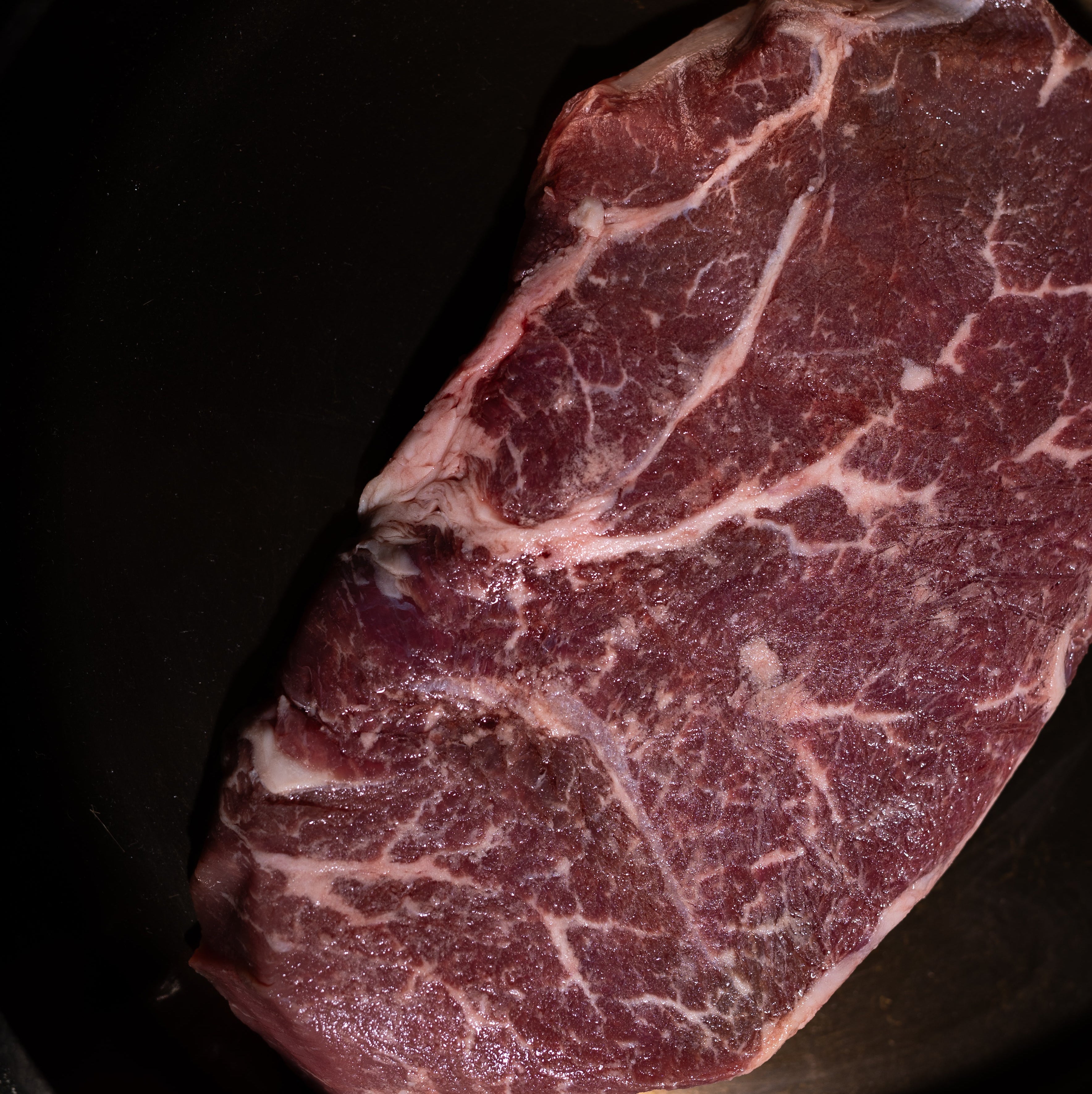 A raw, marbled beef steak, likely Wagyu, resting inside a black cast iron skillet.