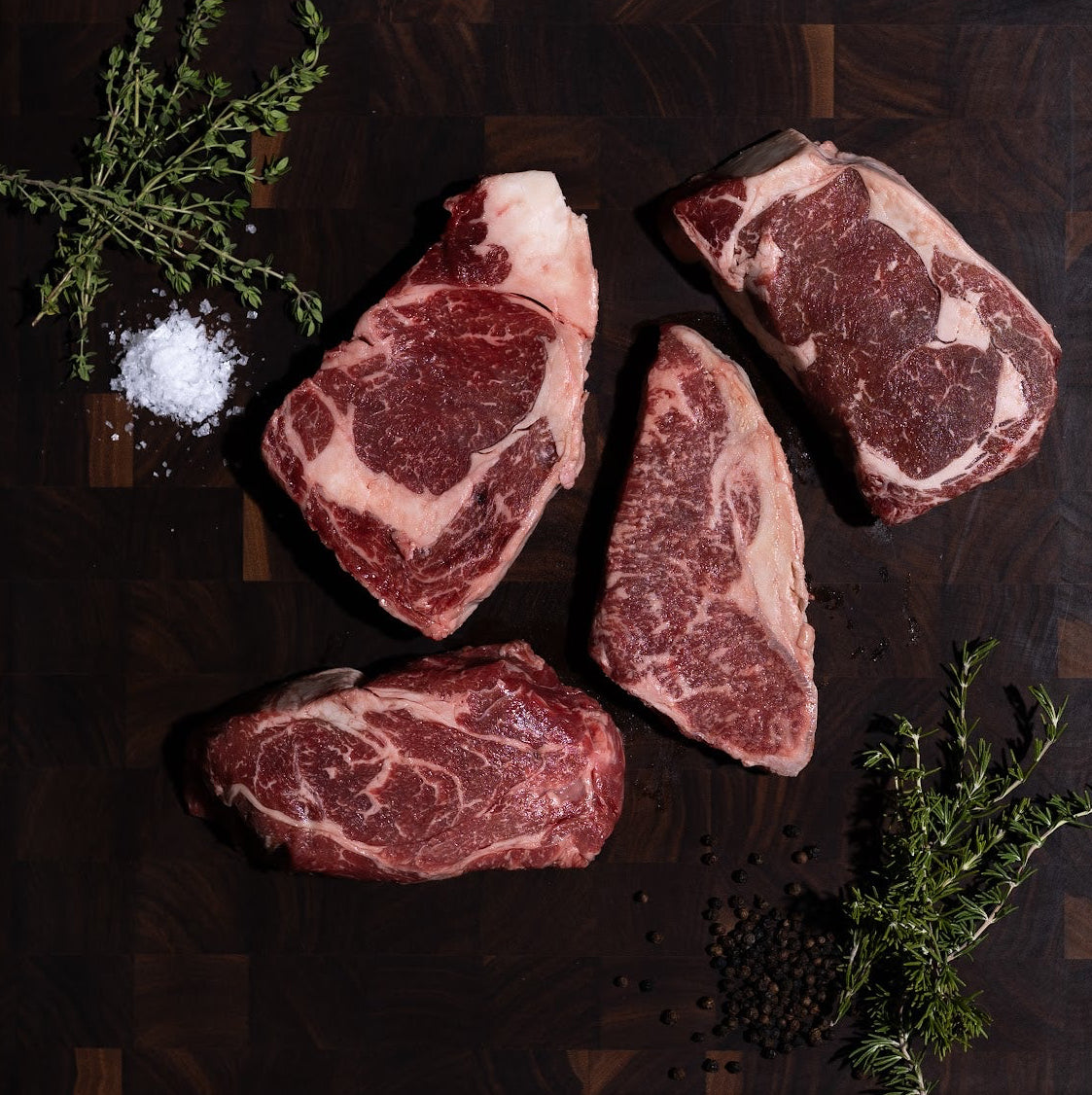 Raw wagyu beef steaks on a dark wooden cutting board with herbs and salt.